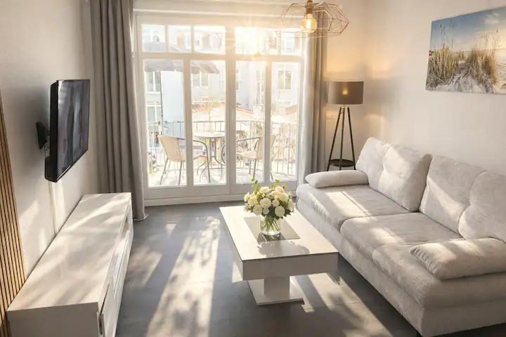 Bright vacation rental living room with a light sofa, coffee table with flowers and doors opening to a balcony